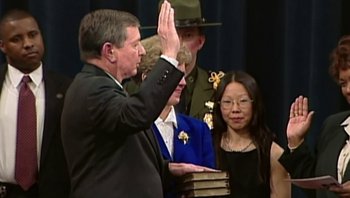 Movie still from “Fahrenheit 9/11” (2004), directed by Michael Moore – A man is taking his oath in front of a group of people; Medium shot, Low angle