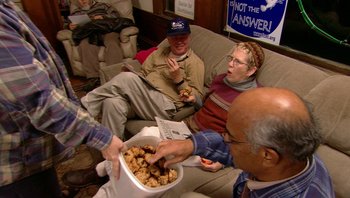 Movie still from “Fahrenheit 9/11” (2004), directed by Michael Moore – A group of people sitting on top of a couch eating food; Wide shot, High angle