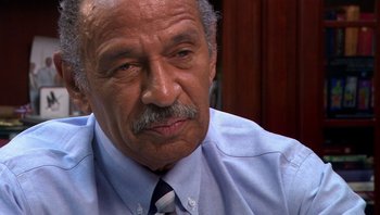 Movie still from “Fahrenheit 9/11” (2004), directed by Michael Moore – An older man wearing a blue dress shirt and a tie; Close Up shot, High angle