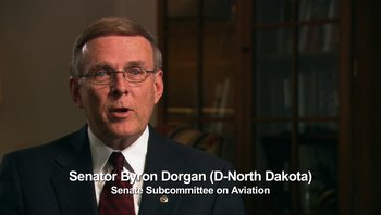 Movie still from “Fahrenheit 9/11” (2004), directed by Michael Moore – A man wearing a suit and tie and glasses; Medium shot, Over the shoulder angle