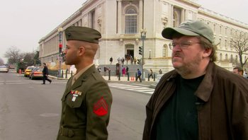 Movie still from “Fahrenheit 9/11” (2004), directed by Michael Moore – Two men in military fatigues stand in front of a building; Medium shot, Over the shoulder angle