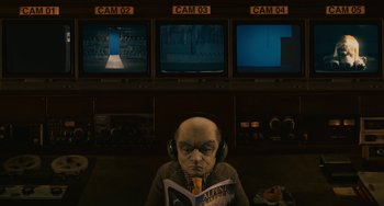 Movie still from “Fantastic Mr. Fox” (2009), directed by Wes Anderson – An old man wearing headphones while reading a book in front of three monitors; Medium shot, High angle