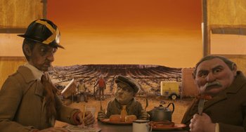 Movie still from “Fantastic Mr. Fox” (2009), directed by Wes Anderson – A man sitting at a table with a plate of hot dogs; Wide shot, High angle
