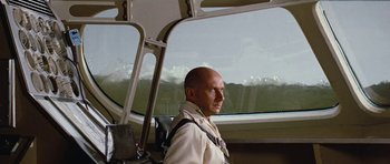 Movie still from “Fantastic Voyage” (1966), directed by Richard Fleischer – A bald man in a white shirt is sitting in a bus; Medium shot, Low angle
