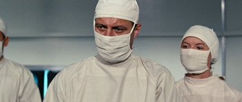 Movie still from “Fantastic Voyage” (1966), directed by Richard Fleischer – A man wearing a surgical gown and a surgical mask; Close Up shot, Low angle