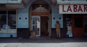 Movie still from “Fat City” (1972), directed by John Huston – A man standing in front of a building on a street; Wide shot, Low angle