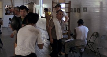 Movie still from “Fat City” (1972), directed by John Huston – A group of people standing around in a room; Wide shot, Over the shoulder angle