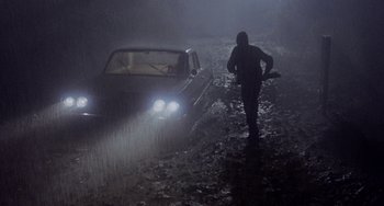 Movie still from “Fat City” (1972), directed by John Huston – A man walking on a wet road near a car in the rain; Wide shot, High angle