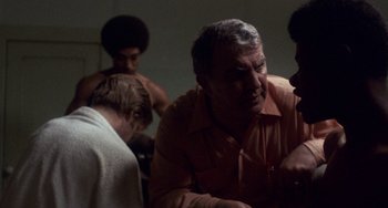 Movie still from “Fat City” (1972), directed by John Huston – An older man in an orange shirt is talking to a group of young men; Close Up shot, Over the shoulder angle