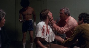 Movie still from “Fat City” (1972), directed by John Huston – A man with blood all over his face is being examined by two other men; Medium shot, Low angle