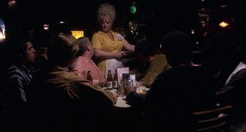 Movie still from “Fat City” (1972), directed by John Huston – A group of people sitting at a table with drinks; Medium shot, Over the shoulder angle