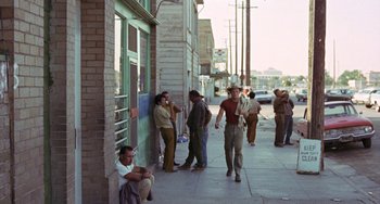 Movie still from “Fat City” (1972), directed by John Huston – A group of men standing on a sidewalk near a building; Wide shot, High angle