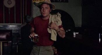 Movie still from “Fat City” (1972), directed by John Huston – A man holding a beer and wearing a hat; Medium shot, Low angle