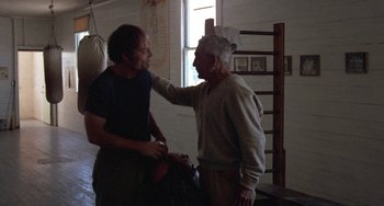 Movie still from “Fat City” (1972), directed by John Huston – A man and an older man are talking in a room; Medium shot, Over the shoulder angle