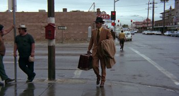 Movie still from “Fat City” (1972), directed by John Huston – A man walking down the street holding a briefcase; Wide shot, Low angle