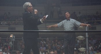 Movie still from “Fat City” (1972), directed by John Huston – Two men in suits are standing in front of an audience; Wide shot, Low angle