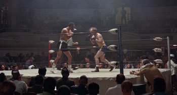 Movie still from “Fat City” (1972), directed by John Huston – Two men are boxing in a boxing ring while people watch; Wide shot, High angle