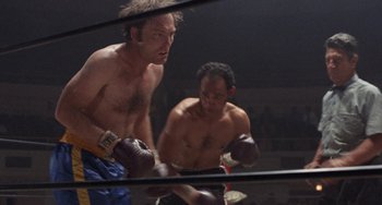 Movie still from “Fat City” (1972), directed by John Huston – Two boxers in a boxing ring one of them is wearing a blue shorts and the other is wearing a red and white boxing glove; Medium shot, Low angle
