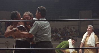Movie still from “Fat City” (1972), directed by John Huston – Two men in a boxing ring fighting for a woman in a green dress; Medium shot, Over the shoulder angle