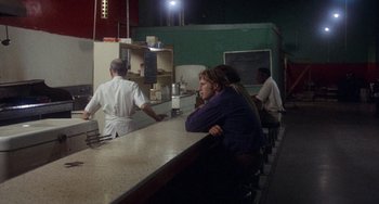 Movie still from “Fat City” (1972), directed by John Huston – A group of people standing around a counter; Wide shot, Over the shoulder angle