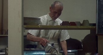 Movie still from “Fat City” (1972), directed by John Huston – An older man in a white shirt is pouring something in a pot; Medium shot, High angle