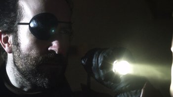 Movie still from “Father's Day” (2011), directed by Conor Sweeney – A man with a beard wearing a pair of eye glasses and holding a flashlight; Close Up shot, Low angle