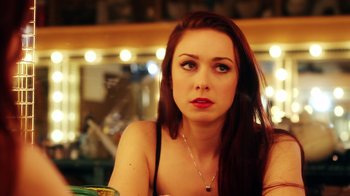 Movie still from “Father's Day” (2011), directed by Conor Sweeney – A beautiful young lady sitting at a table in front of lights; Close Up shot, Over the shoulder angle
