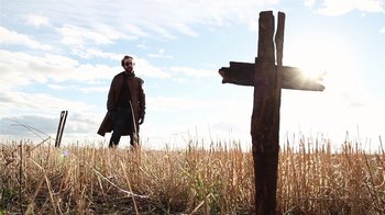 Movie still from “Father's Day” (2011), directed by Conor Sweeney – A man standing next to a wooden cross in a field; Wide shot, Low angle