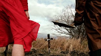 Movie still from “Father's Day” (2011), directed by Conor Sweeney – A woman in a red dress standing next to a cross; Wide shot, Low angle