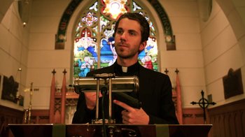 Movie still from “Father's Day” (2011), directed by Conor Sweeney – A man in a priest's outfit standing in front of an organ; Medium shot, Low angle