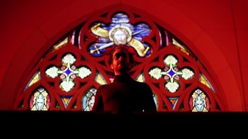 Movie still from “Father's Day” (2011), directed by Conor Sweeney – A man standing in front of a stained - glass window; Medium shot, Low angle