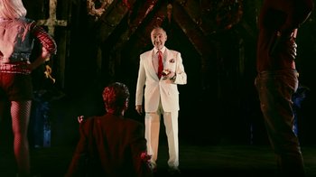Movie still from “Father's Day” (2011), directed by Conor Sweeney – A man in a white suit and a red tie standing in front of a woman; Medium shot, Over the shoulder angle