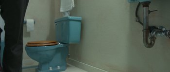 Movie still from “Faults” (2014), directed by Riley Stearns – A toilet that is sitting in a bathroom next to a wall; Extreme Close Up shot, Overhead angle