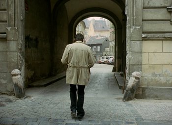 Movie still from “Faust” (1994), directed by Jan Svankmajer – An older man walking down a street in a trench coat; Wide shot, High angle