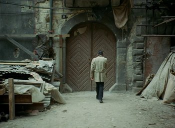 Movie still from “Faust” (1994), directed by Jan Svankmajer – A man walking down a street in front of an old building; Wide shot, High angle