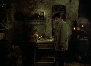 Movie still from “Faust” (1994), directed by Jan Svankmajer – A man standing next to a table in a dimly - lit room; Medium shot, High angle