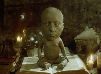 Movie still from “Faust” (1994), directed by Jan Svankmajer – A clay sculpture of a man sitting on top of an open book; Medium shot, High angle