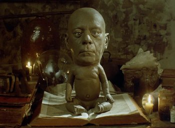 Movie still from “Faust” (1994), directed by Jan Svankmajer – A statue of an old man sitting on top of an open book; Medium shot, High angle