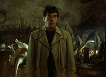 Movie still from “Faust” (1994), directed by Jan Svankmajer – A man wearing a trench coat standing in a room; Medium shot, Over the shoulder angle