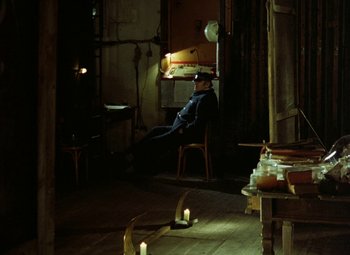 Movie still from “Faust” (1994), directed by Jan Svankmajer – A man sitting on a chair in a room with candles; Wide shot, High angle