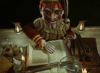 Movie still from “Faust” (1994), directed by Jan Svankmajer – A clown that is sitting at a table; Medium shot, Low angle