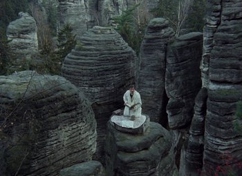 Movie still from “Faust” (1994), directed by Jan Svankmajer – A man sitting on top of a rock in the middle of a forest; Extreme Wide shot, High angle