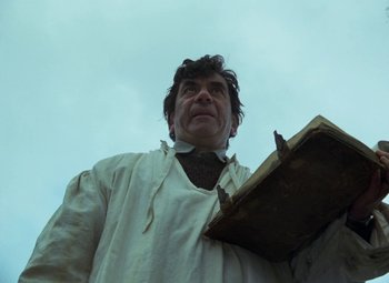 Movie still from “Faust” (1994), directed by Jan Svankmajer – A man holding an open book while wearing a white shirt; Medium shot, Low angle