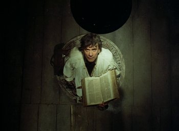 Movie still from “Faust” (1994), directed by Jan Svankmajer – A man sitting on the ground holding a book; Medium shot, Overhead angle
