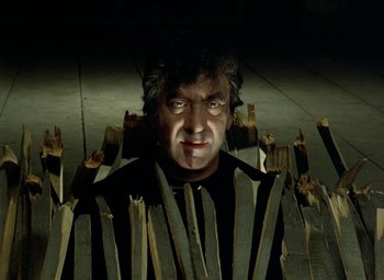 Movie still from “Faust” (1994), directed by Jan Svankmajer – A man is surrounded by wooden sticks in a dark room; Close Up shot, Low angle