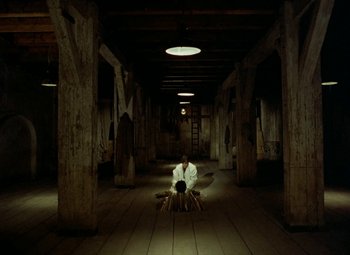 Movie still from “Faust” (1994), directed by Jan Svankmajer – A man sitting on a chair inside of a building; Extreme Wide shot, High angle