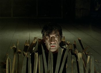 Movie still from “Faust” (1994), directed by Jan Svankmajer – A man with a bunch of wooden sticks in front of him; Medium shot, Low angle