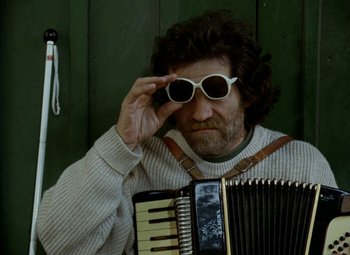 Movie still from “Faust” (1994), directed by Jan Svankmajer – A man wearing sunglasses and holding an accordion; Medium shot, Low angle