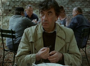 Movie still from “Faust” (1994), directed by Jan Svankmajer – A man sitting in front of a group of people at a table; Close Up shot, Over the shoulder angle