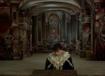 Movie still from “Faust” (1994), directed by Jan Svankmajer – A woman sitting at a table in a room with columns; Wide shot, Low angle